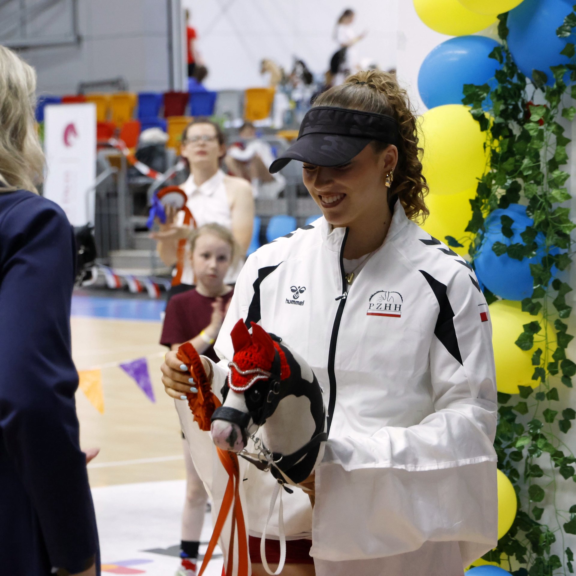 Usměvavá medailistka v týmové bundě drží černého Hobby Horse koně s červenou hřívou při vyhlášení vítězů mistrovství Evropy.